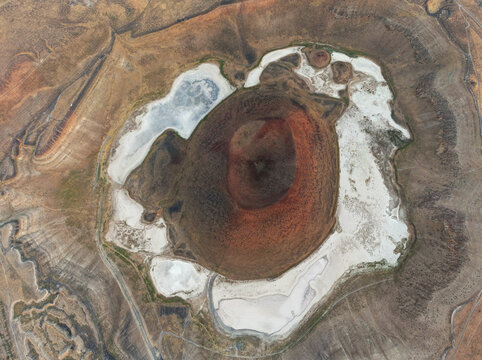Aerial view of Lake Meke, a volcanic crater lake featuring a distinct red and brown center surrounded by white salt deposits and arid terrain in Karapinar, Konya, Turkiye.