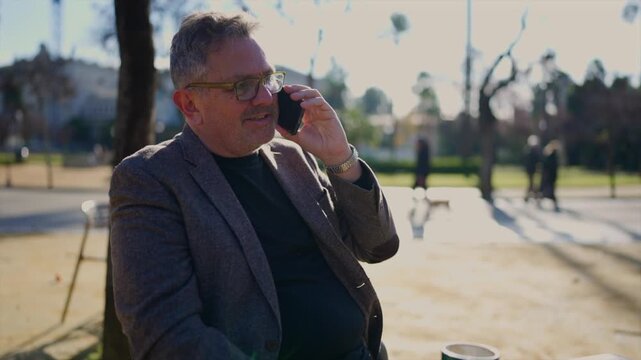 Mature businessman talking on smartphone in a sunny park