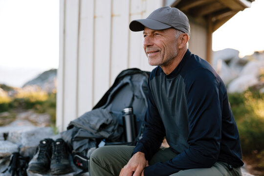 An older man with a joyful smile sits with his organized gear, radiating excitement for the outdoor adventure ahead, embodying the spirit of exploration and appreciation for nature.