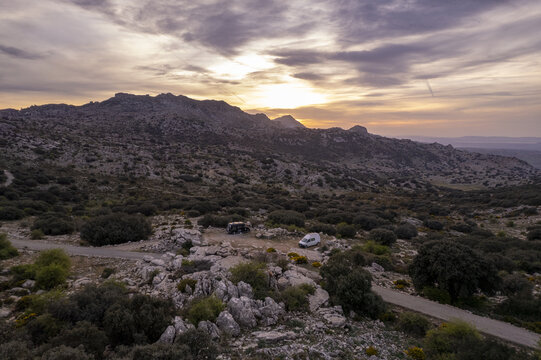 Aerial view of Torcal Antequera karst landscape with rocky formations, shrubs, and parked camper vans at sunset in Province of Malaga, Andalusia, Spain.