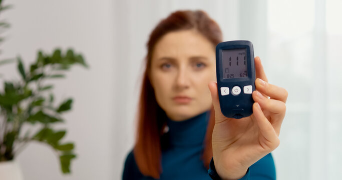 A woman sits at a table checking her glucometer. She receives a reading of 111 mg dL, indicating high blood sugar. She reflects on her diabetes management.
