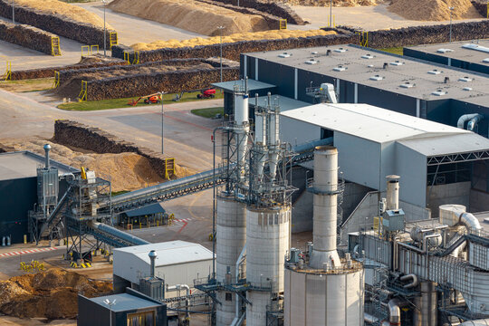 View of a large particleboards production plant with industrial silos, conveyor systems, and piles of wood chips in Poland.