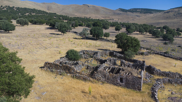 Aerial view of stone ruins in a rural landscape with dry grass, scattered trees, and stone walls set against rolling hills in Emirgazi, Konya, Turkiye.