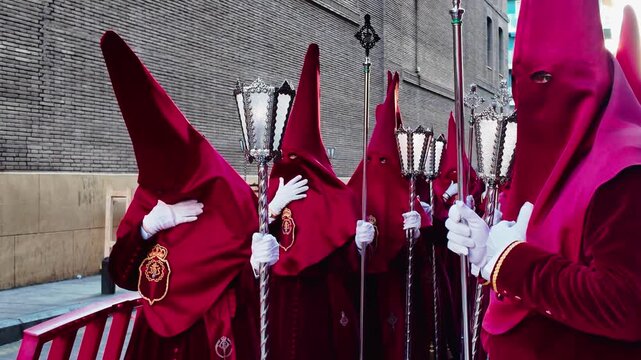 Catholic penitents wearing traditional crimson velvet robes and pointed hoods carrying ornate silver lanterns during a solemn Easter week procession on Holy Monday in the streets of Murcia Spain