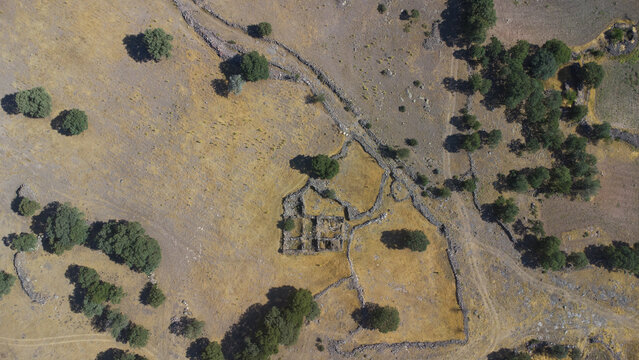 Aerial view of ancient stone ruins surrounded by dry golden fields, scattered trees, and historic stone boundary walls in Emirgazi, Konya, Turkiye.
