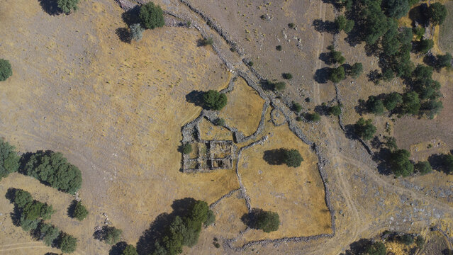 Aerial view of ancient stone ruins surrounded by dry fields, scattered trees, and historic stone walls in the rural landscape of Emirgazi, Konya, Turkiye.