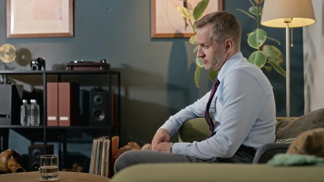 Middle-aged Caucasian man sitting on sofa during therapy session, talking and expressing anxiety. Footage is ideal for mental health awareness campaigns and counseling services