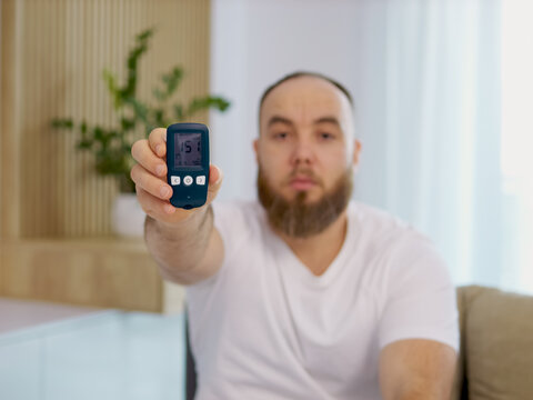 A man holds up a glucometer with a reading of 151 mg dL, showing a high blood sugar level. This reading is significant for diabetes management and awareness.