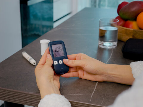 A woman in the kitchen is reviewing her blood glucose meter log. She is analyzing past blood glucose results to effectively manage her health.