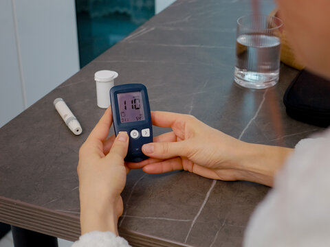 Hands of a woman in the kitchen swipe through the glucometer diary. She reviews past blood sugar results to manage her health effectively.