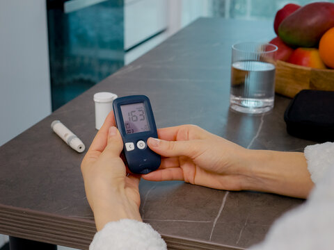 Hands of a woman in a kitchen check the history of blood sugar results using a glucometer diary. The activity shows the importance of monitoring glucose levels daily.