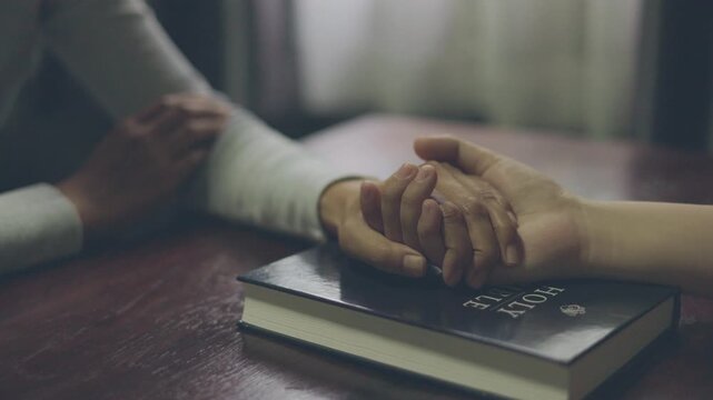 Two people holding hands in prayer, sharing faith, hope, love, peace, and spiritual support in a quiet room.