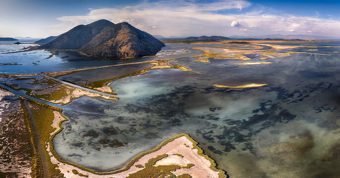 Aerial view of the Korission Lagoon featuring shallow turquoise waters, sandy banks, and a large mountain under a blue sky in Mesongi, Greece.