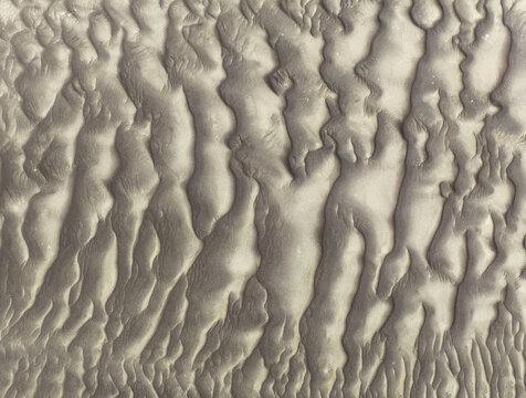 Aerial view of the intricate sand dune patterns of the Skeleton Coast, showcasing rhythmic ridges and textures formed by wind in the Kunene Region, Namibia.