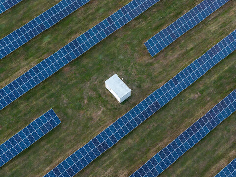 Aerial view of a solar farm with rows of photovoltaic panels arranged in a field surrounding a small white utility building in Poland.