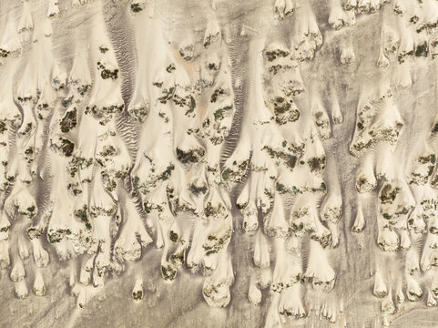 Aerial view of the Skeleton Coast featuring intricate sand dunes with patches of desert vegetation and wind-swept patterns in Kunene Region, Namibia.