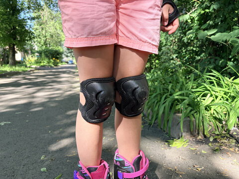 A girl's legs in protective knee pads and roller skates on asphalt