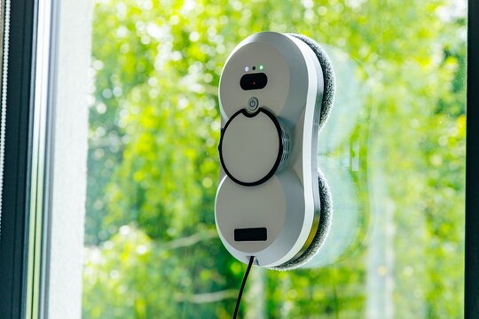 Window cleaning robot positioned on glass with green outdoor foliage in the background