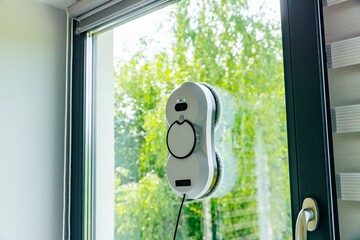 Obraz premium Window cleaning robot actively scrubbing glass surface with bright green foliage in background