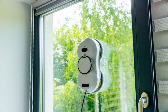 Window cleaning robot actively scrubbing glass surface with bright green foliage in background
