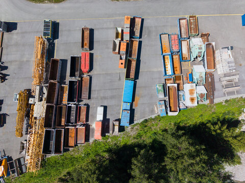 Aerial view of the Upper Engadine Wastewater Treatment Plant storage yard featuring rows of metal containers and construction equipment on an asphalt surface in S-chanf, Grisons, Switzerland.