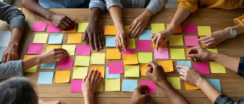 Innovation in action a diverse group collaborates over vibrant sticky notes in an overhead flat lay perspective. Ideal for agile, startup culture, design thinking, and team strategy.