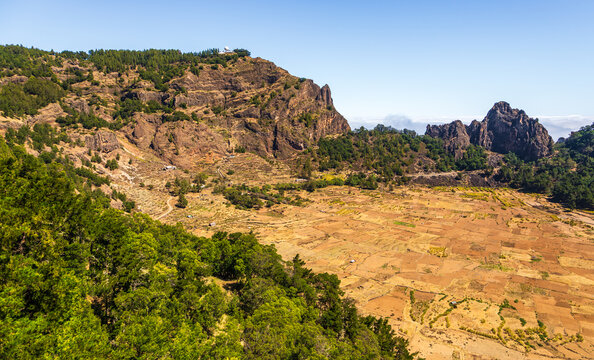 Aerial view of Cova Crater Panoramic Viewpoint featuring terraced fields, rugged volcanic rock formations, and pine forests in Faja de Cima, Porto Novo, Cabo Verde.