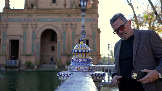 Elegant middle-aged tourist filming with smartphone at plaza de espa&ntilde;a in seville