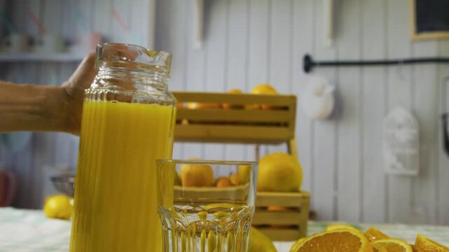 Slow motion shot of juice from pitcher being poured into glass near orange slices