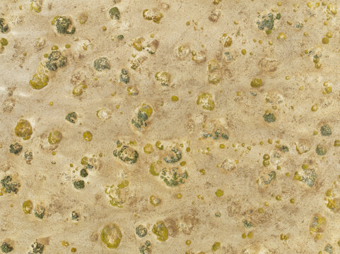 Aerial view of the Skeleton Coast featuring textured sandy terrain dotted with small patches of green vegetation in the Kunene Region, Namibia.