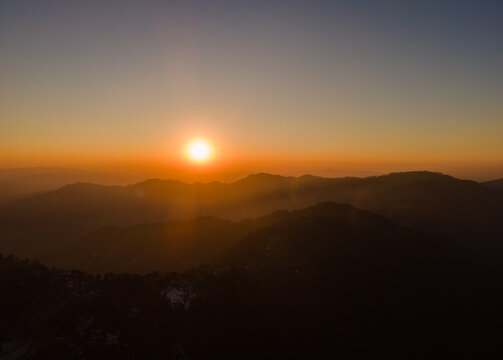 Aerial view of the sun setting over the silhouetted mountain ranges of the Himalayan foothills in AJK, Pakistan.
