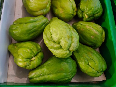 Fresh green chayote squashes with wrinkled skins are arranged together inside a green display tray at a grocery store.