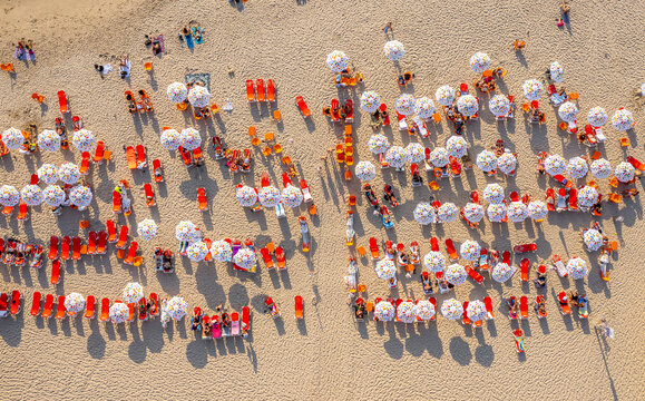 Aerial view of Tel Aviv Beach with rows of white umbrellas and orange sun loungers on the sand, with people relaxing under the sun in Tel Aviv-Yafo, Tel Aviv District, Israel.