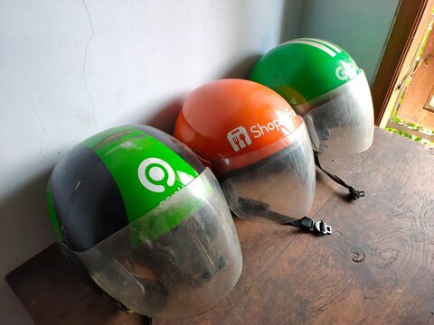 Malang, Indonesia - July 11, 2026: Three helmets used by Indonesian ride-hailing and delivery services: Grab, ShopeeFood, and Gojek. Helmet for rider. Gig worker. Freelancer. Freelance.