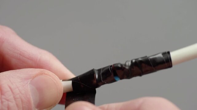 Hands wrap tape layers around cable for enhanced strength and longevity. Carefully sealing cable with layers of tape to improve durability and safety for daily use
