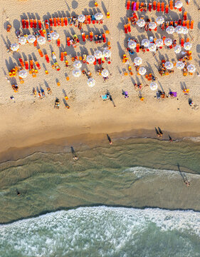 Aerial view of Tel Aviv Beach with rows of colorful umbrellas, sun loungers, and people relaxing on the sand by the Mediterranean Sea in Tel Aviv-Yafo, Tel Aviv District, Israel.
