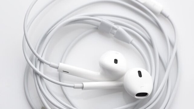 White wired in-ear headphones with USB Type-C connector rotating slowly on a seamless white background.	