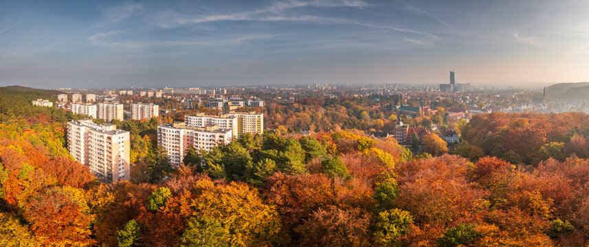 Aerial view of the Oliwa district in Gdansk, featuring residential apartment blocks surrounded by vibrant autumn-colored forests under a clear sky. Gdansk, Pomeranian Voivodeship, Poland.