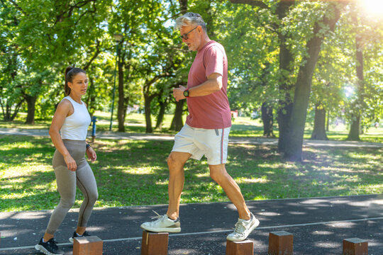 Senior man practicing agility step training on wooden balance posts under the guidance of a fitness coach to improve coordination, balance, mobility, and functional fitness.