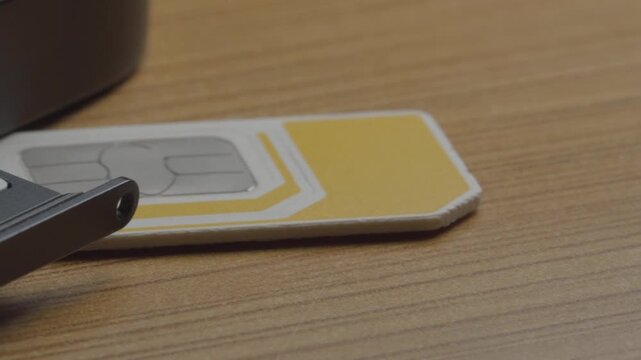Closeup of SIM card tray ejecting from smartphone with nano SIM cards. Mobile device shows dual SIM slot during card installation on wooden surface
