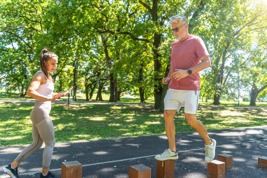 Senior man performing a coordination and balance exercise on outdoor wooden posts with professional coaching to enhance stability, lower body strength, and movement confidence.