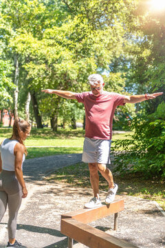 Senior man performing a balance training exercise on a narrow beam with professional coaching to develop coordination, lower body stability, confidence, and functional mobility.