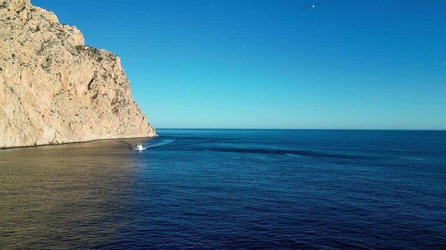 Aerial view of the Penyal d'Ifac limestone cliff rising from the Mediterranean Sea with a small boat leaving a wake in Calp, Valencian Community, Spain.