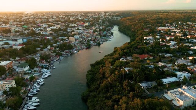 Aerial view of the Chavon River with docked boats along the bank, surrounded by urban buildings and lush tropical vegetation in La Romana, La Romana Province, Dominican Republic.