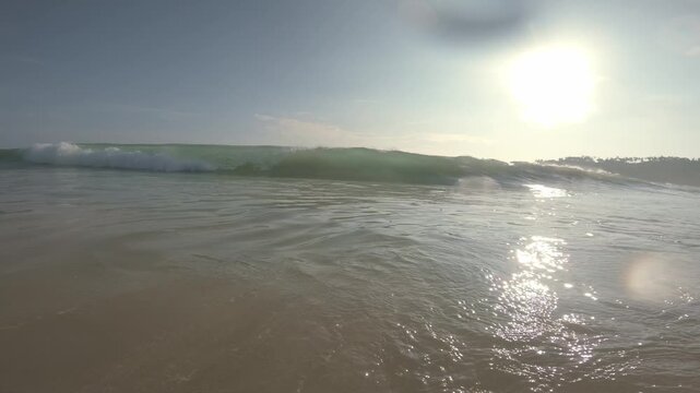 A sunlit tropical wave rolls toward a low waterline camera and breaks across the lens, briefly submerging the view in foamy surf off Mirissa, Sri Lanka.