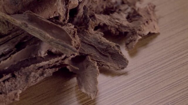 Macro close up of dried tree bark resting on wooden surface. Rough fibrous texture, layered wood and natural brown tones fill the frame in fine detail