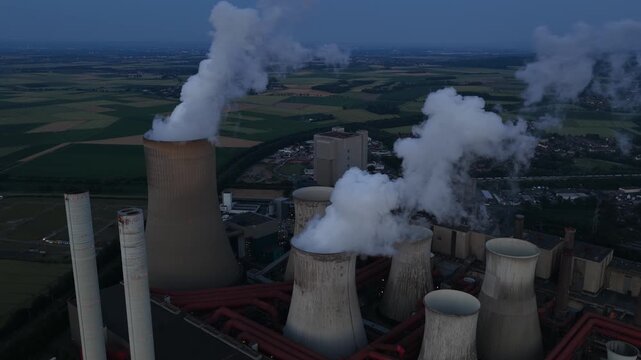 Aerial view of Power Plant Niederausem in Germany at dusk, showing a massive fossil fuel station with smoking cooling towers and industrial energy infrastructure.