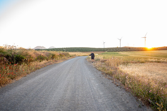Man hitchhiking on dusty country road at sunset
