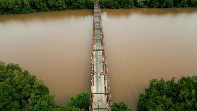 Aerial view of the historic rusty bridge spanning the brown waters of Rio Soco surrounded by lush tropical vegetation in San Pedro de Macoris, San Pedro de Macoris, Dominican Republic.