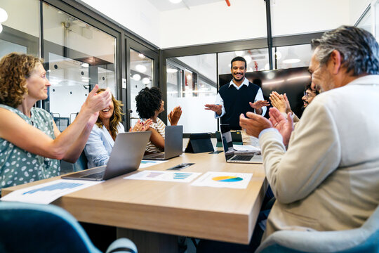 Group of happy businesspeople clapping hands to a successful male speaker during a presentation in a modern coworking office
